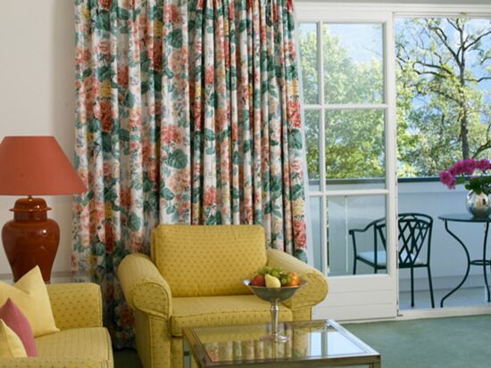 A hotel room with a seating set and table, with a balcony overlooking the lake