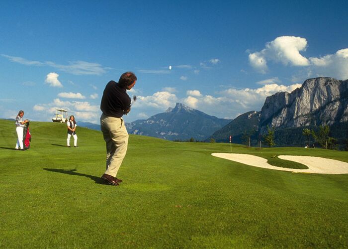 Ein Man schlägt den Golfball ab und zwei Frauen sehen ihn zu