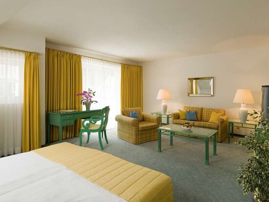 A hotel room with a seating set and table, with a balcony overlooking the lake