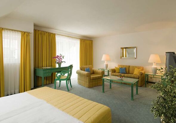 A hotel room with a seating set and table, with a balcony overlooking the lake