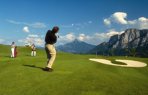 Ein Man schlägt den Golfball ab und zwei Frauen sehen ihn zu