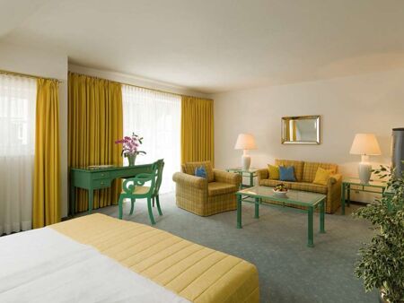 A hotel room with a seating set and table, with a balcony overlooking the lake