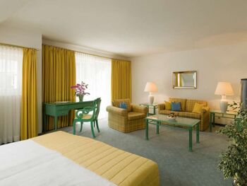 A hotel room with a seating set and table, with a balcony overlooking the lake